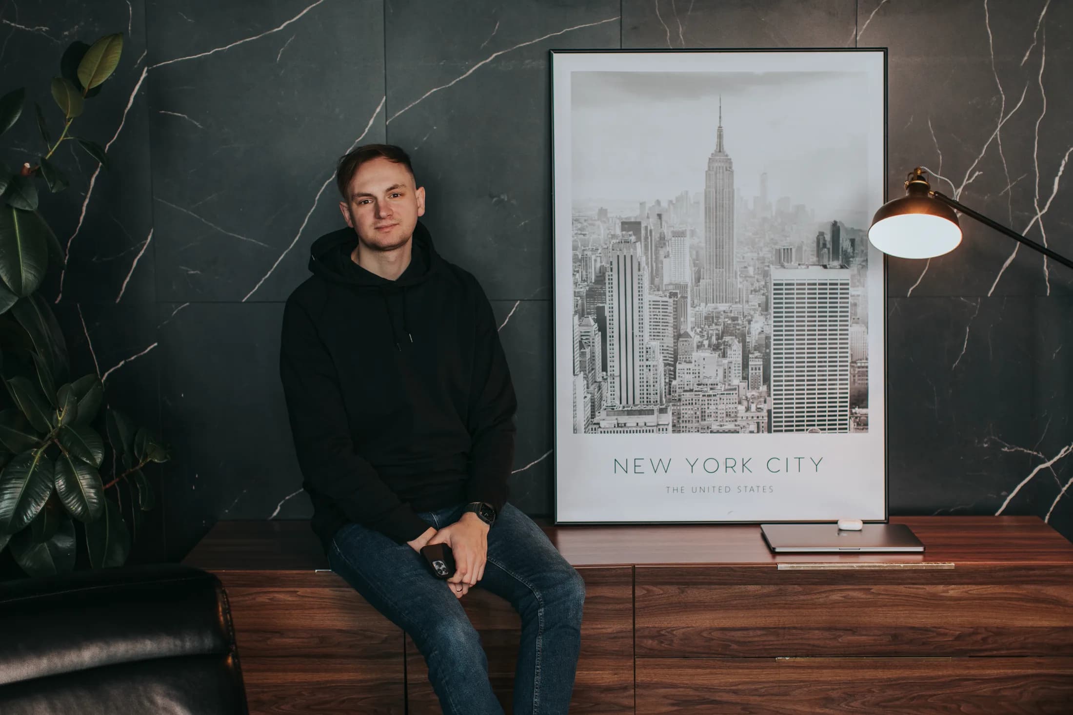 Pavel Bileush in a dark studio interior with a New York City print.